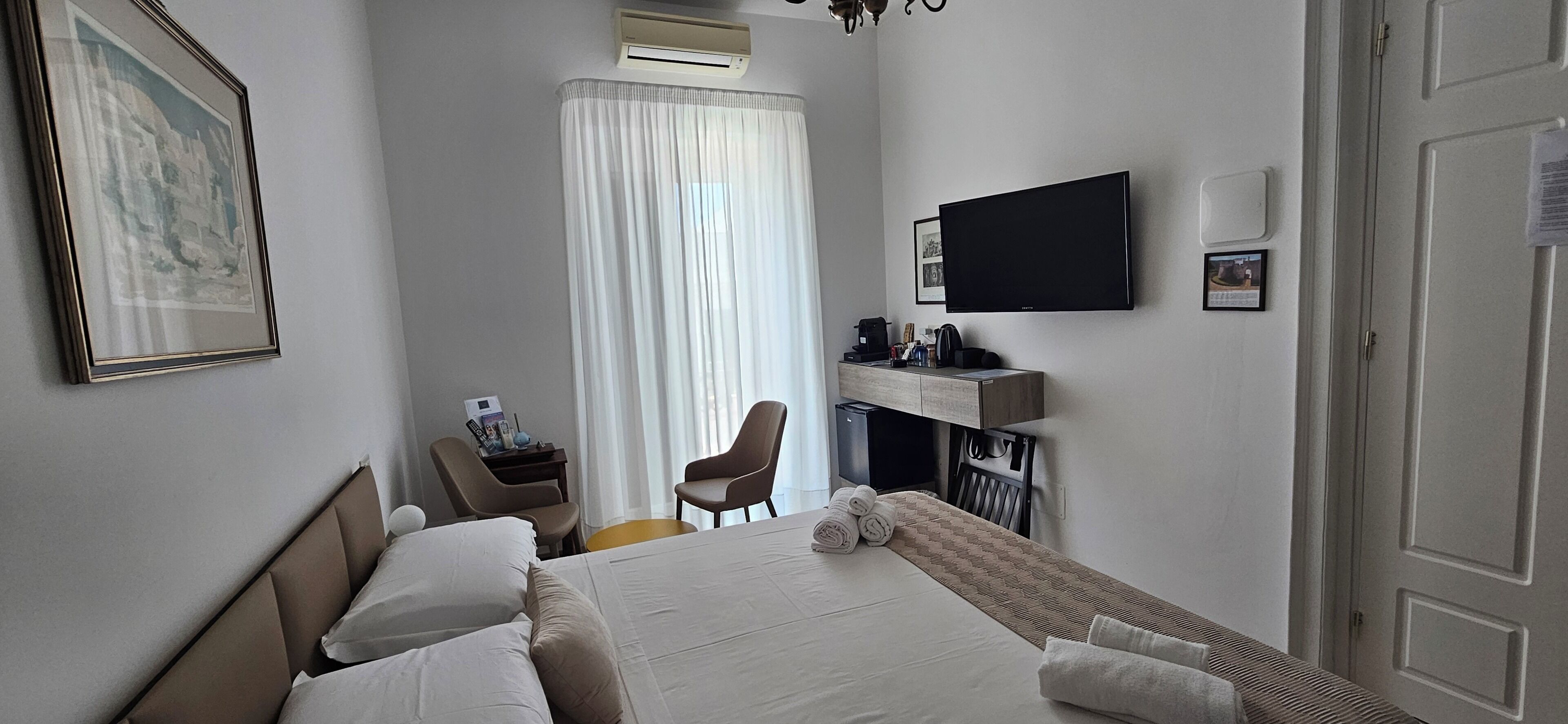 A hotel room with a bed, a desk, a chair, a TV, and a door.