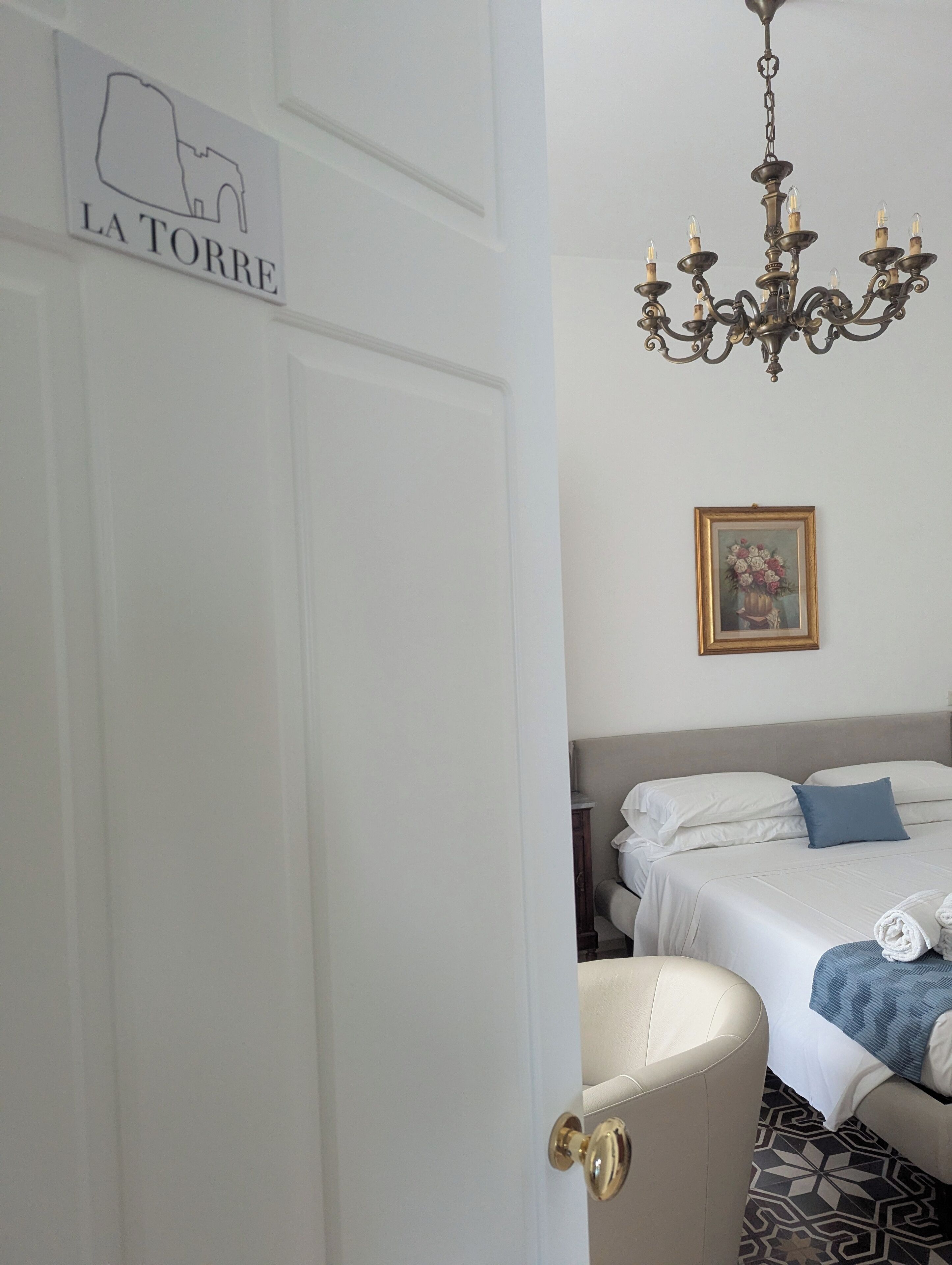 A hotel room with a bed, a chair, a chandelier, and a sign reading "LA TORRE".