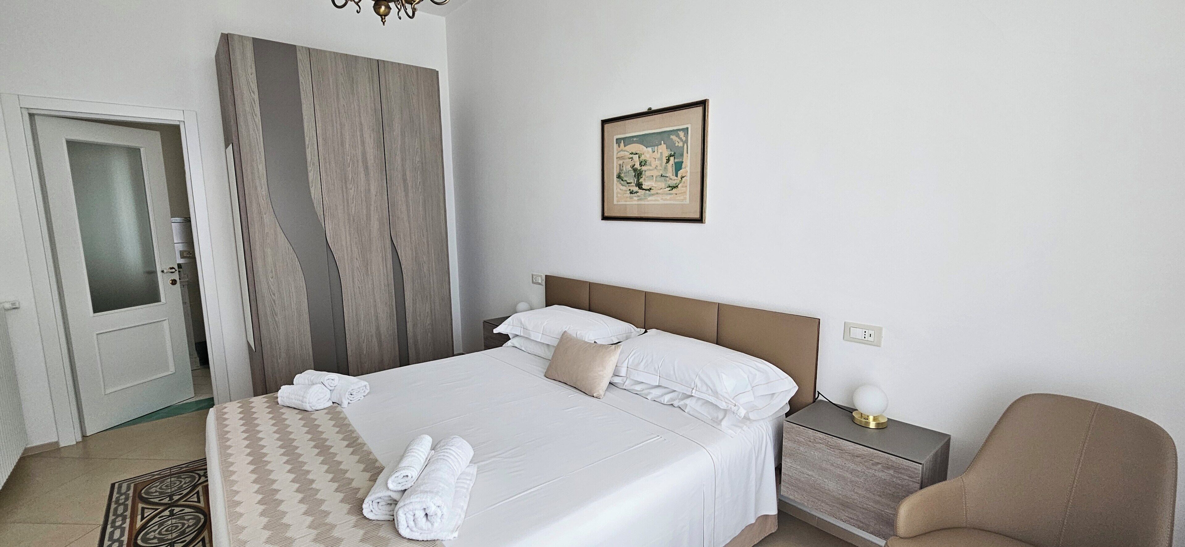Ein Hotelzimmer mit einem Bett, einem Nachttisch, einem Stuhl, einer Tür und einem Wandbild.