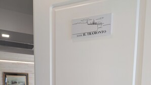 A hotel room with a bed, a painting on the wall, and a sign above the door reading 'SUITE IL TRAMONTO.'