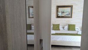 A hotel room with a bed, a nightstand, a framed picture on the wall, and a view of the sea.