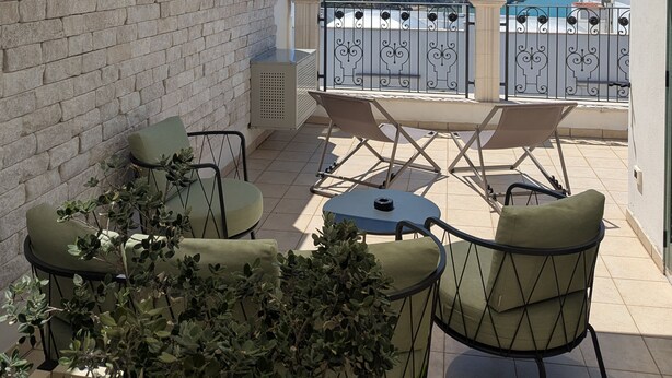 A balcony with a view of the sea, featuring a brick wall, a metal railing, and outdoor furniture.