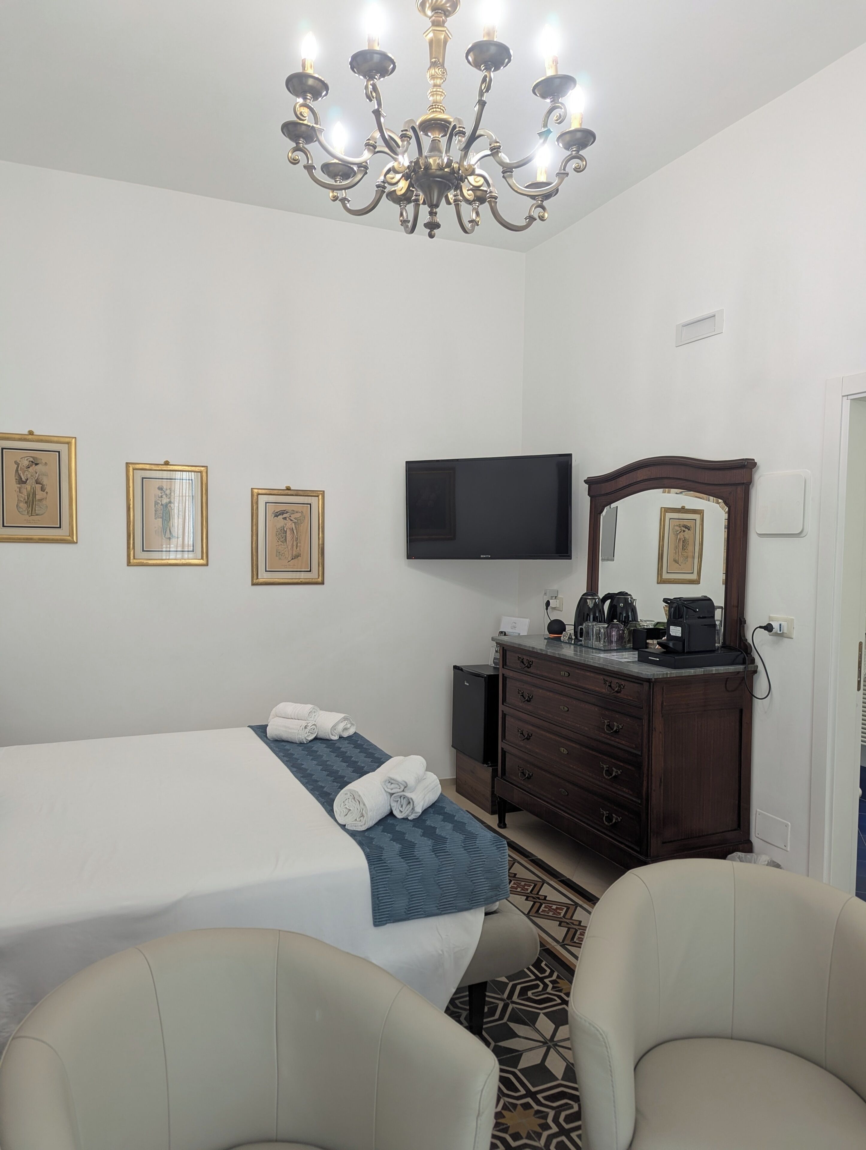 A hotel room with a bed, a dresser, a television, and a chandelier.