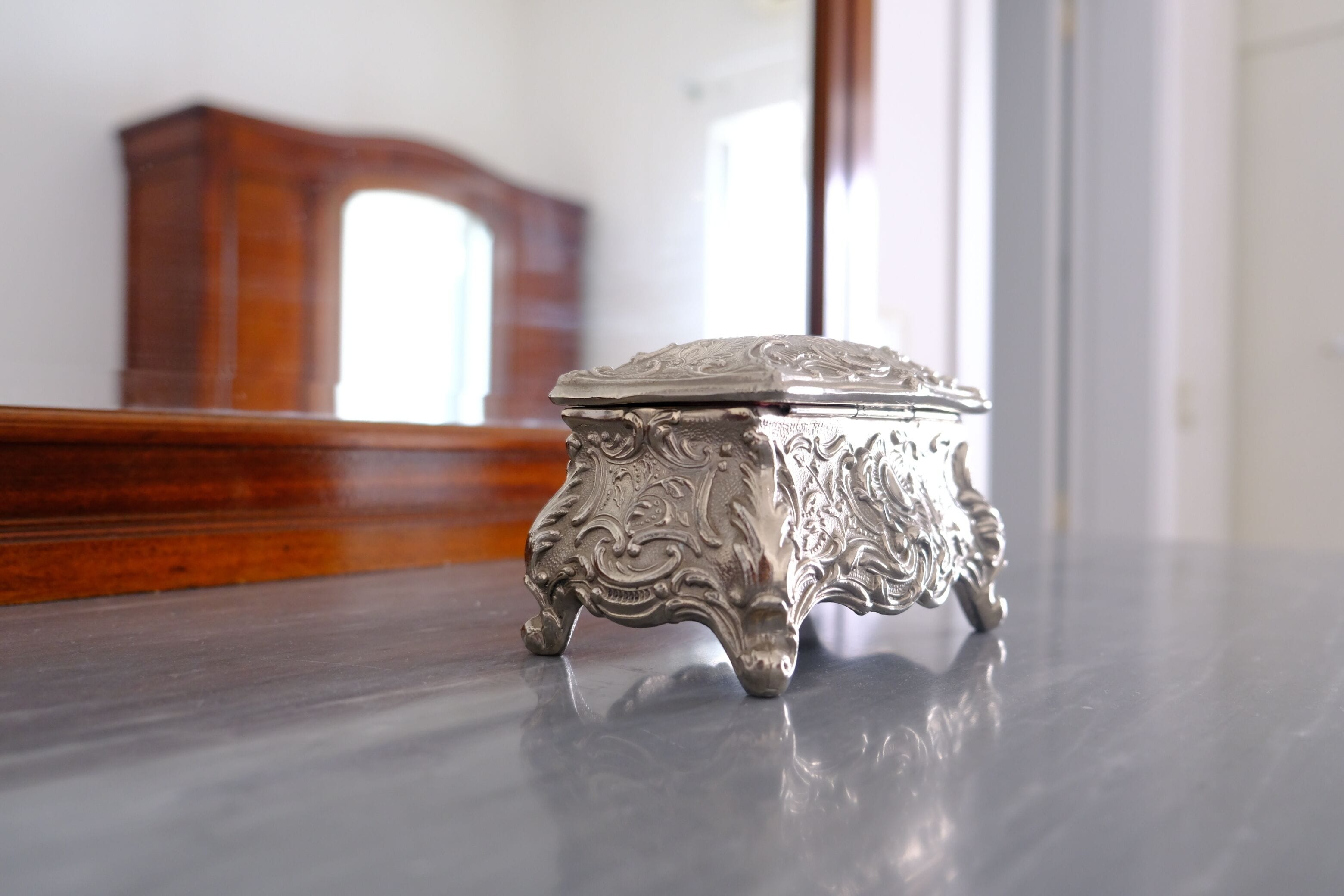 Uma caixa prateada e ornamentada sobre uma superfície refletora.
