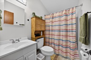 Een badkamer met een wit wastafelmeubel, een houten kastje, een douchegordijn met strepen en een groene handdoek.