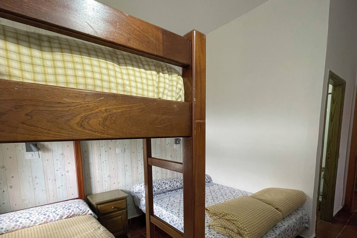 A room with two bunk beds, a small bedside table, and a plain wall.