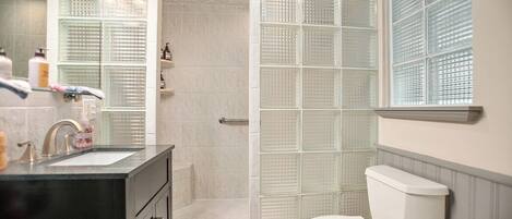 A bathroom with a glass shower enclosure, a white toilet, and a black vanity with a sink.