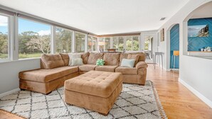 A spacious living room with a large sectional sofa, a matching ottoman, and a view of the outdoors through large windows. - Lakefront Getaway 10 minutes from downtown Deland (DeLand)