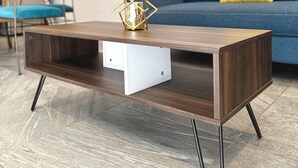 Un salon moderne avec une table basse en bois, un canapé bleu agrémenté d’un coussin jaune et un fauteuil en osier.