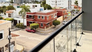 Une vue depuis un balcon donnant sur un paysage urbain, avec des bâtiments modernes, un chantier de construction et une rue où circulent des voitures et des motos.