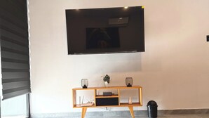 Un salon moderne avec un téléviseur à écran plat fixé au mur, une console en bois agrémentée d’objets décoratifs et une table basse avec un élément central en verre aux motifs géométriques.