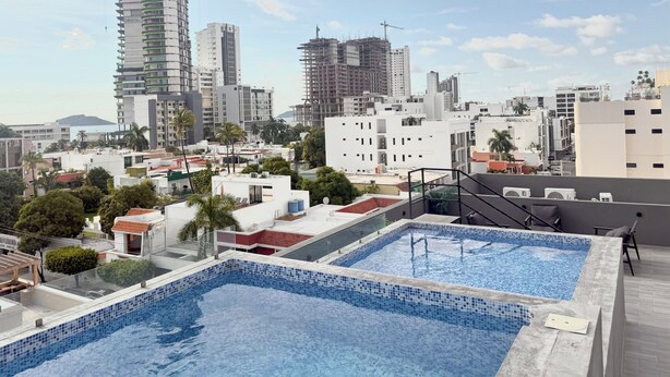 Une piscine sur le toit offrant une vue panoramique sur la ville, avec notamment des immeubles de grande hauteur et des chantiers de construction.
