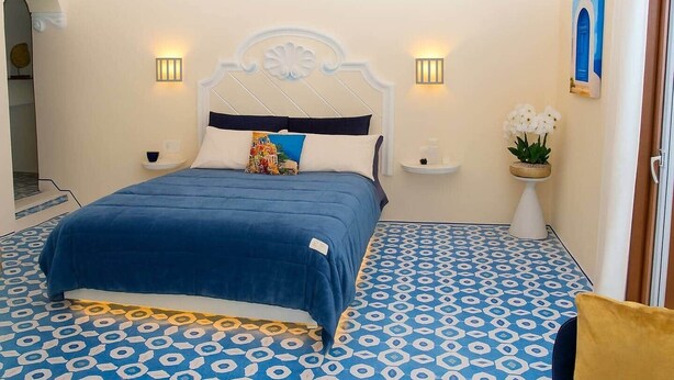 Ein Schlafzimmer mit einem Bett, zwei Nachttischen, einer Stehlampe und einer Wandleuchte sowie einer Zimmerpflanze.