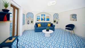Ein modernes Wohnzimmer mit einem blauen Sofa, einem Couchtisch und einem blauen Sessel. Dekorative Regale und ein gemusterter Boden runden den Raum ab.
