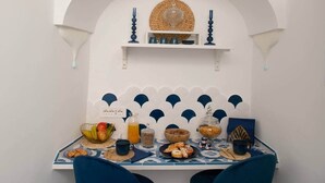 Ein Essbereich in Weiß und Blau gehalten, mit einem Tisch, der mit verschiedenen Speisen und Getränken gedeckt ist, und einer Wand mit einer gezackten Verzierung.