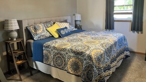 A bedroom with a bed, two bedside tables, a ceiling fan, and a window with curtains.