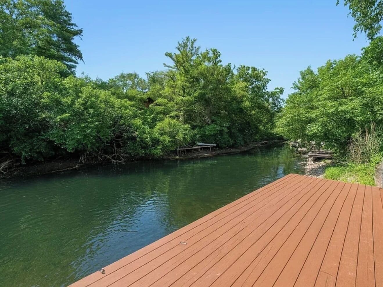 Una terraza de madera con vistas a un río tranquilo, rodeada de abundante vegetación.