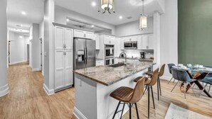 A modern kitchen with white cabinets, stainless steel appliances, and a marble island with bar stools. - Luxury Condo Heart of Downtown / 98/100 Walk Score (Cleveland)