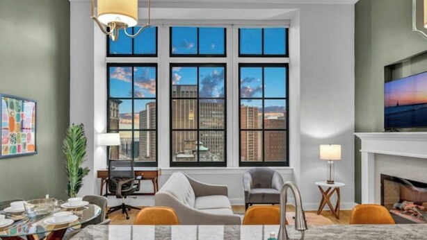 A modern living room with a large window, a fireplace, and a dining area with a glass table. - Luxury Condo Heart of Downtown / 98/100 Walk Score (Cleveland)