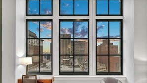 A room with large windows offering a city view, a desk with a chair, and a lamp. - Luxury Condo Heart of Downtown / 98/100 Walk Score (Cleveland)