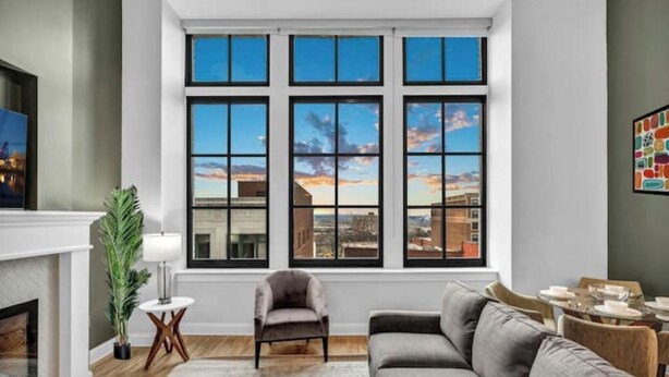 A living room with a large window, a fireplace, a sofa, and a dining area. - Luxury Condo in Playhouse Square: Walkers Paradise (Cleveland)