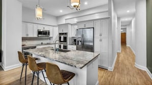 A modern kitchen with white cabinetry, a large island with bar stools, stainless steel appliances, and pendant lighting. - Luxury Condo in Playhouse Square: Walkers Paradise (Cleveland)