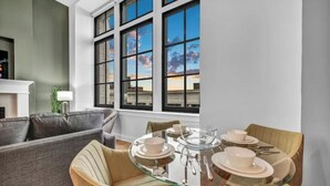 A dining area with a glass table set for four, a grey sofa, and a view of the sky through large windows. - Luxury Condo in Playhouse Square: Walkers Paradise (Cleveland)