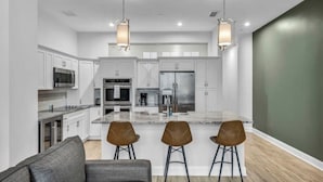 A modern kitchen with white cabinets, stainless steel appliances, and a central island with stools. - Luxury Condo in Playhouse Square: Walkers Paradise (Cleveland)