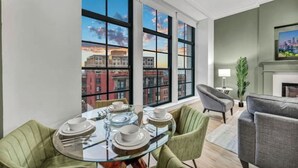 A dining area with a glass table, green chairs, and a view of buildings through large windows. - Stunning Luxury Downtown Condo in Playhouse Square (Cleveland)