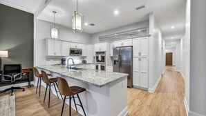 A modern kitchen with white cabinets, a large island, and bar stools. - Stunning Luxury Downtown Condo in Playhouse Square (Cleveland)
