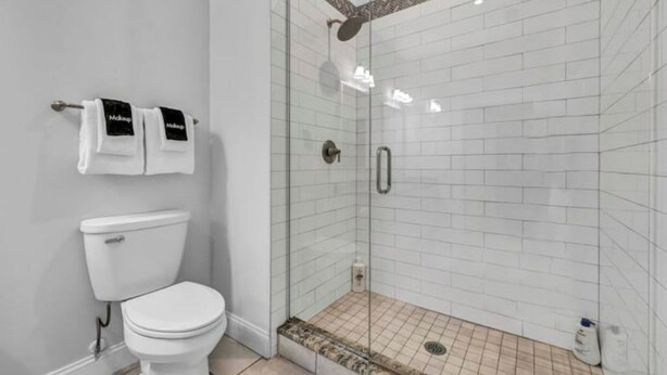 A bathroom with a toilet, a glass-enclosed shower, and white tiled walls. - The Halle Downtown 1BD / FREE Parking/Gym/Security (Cleveland)