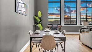 A dining area with a table set for four, a plant, and a view of a cityscape through large windows. - The Halle Downtown 1BD / FREE Parking/Gym/Security (Cleveland)