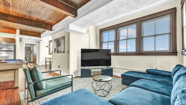Una sala moderna con un televisor grande, sofás azules, una mesa de billar y un techo de madera.