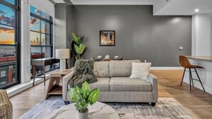 Una sala de estar moderna con un sofá gris, una mesa de centro y un ventanal con vistas a la ciudad.
