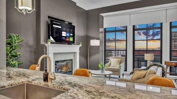 Un salón moderno con un televisor grande, chimenea y vistas de la ciudad a través de amplios ventanales.