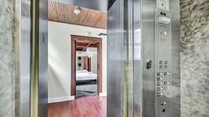Un ascensor con un panel de control y vista a una habitación con cama y piso de madera.