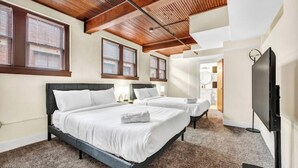 Habitación de hotel con dos camas, vigas de techo de madera, ventanas amplias, un televisor de pantalla plana y piso alfombrado.
