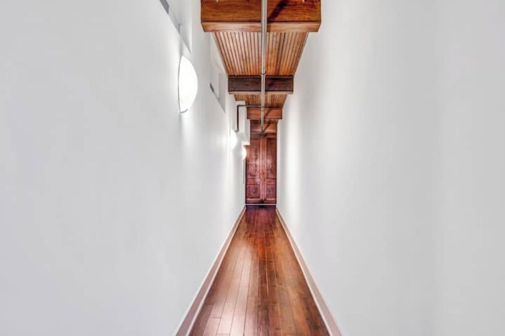 A long, narrow hallway with wooden flooring and a wooden ceiling structure.
