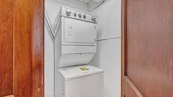 A compact laundry room with a stacked washer and dryer, a wooden door, and a white wall.