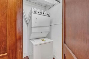A compact laundry room with a stacked washer and dryer, a wooden door, and a white wall. - Urban Industrial Penthouse | Game Room Pool Table (Cleveland)