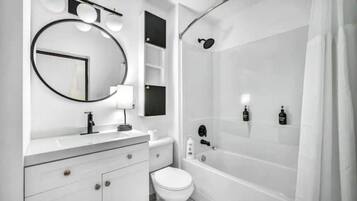 A modern bathroom with a white vanity, a toilet, a bathtub, and a shower.