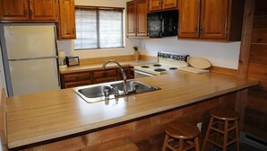 A kitchen with wooden cabinets, a stainless steel sink, a stove, and two stools.