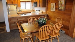 A wooden cabin-style kitchen with a dining table and chairs, a refrigerator, a stove, and a sink.