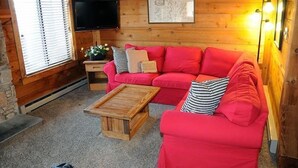A cozy cabin interior with a red sofa, a wooden coffee table, a TV, and a map on the wall.