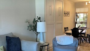 A living room with a grey sofa, a blue armchair, a glass coffee table, a patterned rug, a white cabinet, a lamp, and a window with blinds. - Be cool @ the pool! Quiet & private but near local attractions and conveniences! (Scottsdale)