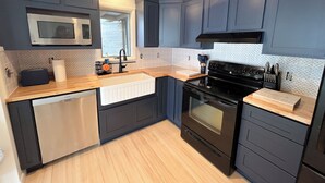 A modern kitchen with dark blue cabinets, a stainless steel microwave, a black stove, and a wooden countertop.