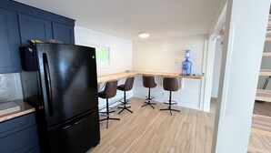 A compact kitchen with a black refrigerator, wooden countertop, and four bar stools.