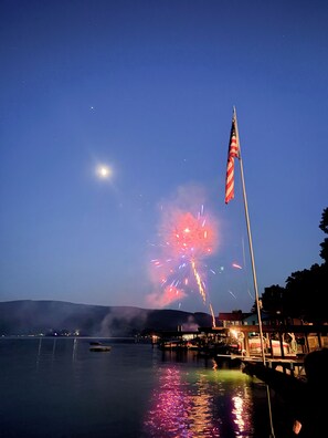 A nighttime view of a waterfront with fireworks, a flag, and a dock. - Hammondsport 100ft lakefront 4 Private Docks (Hammondsport)