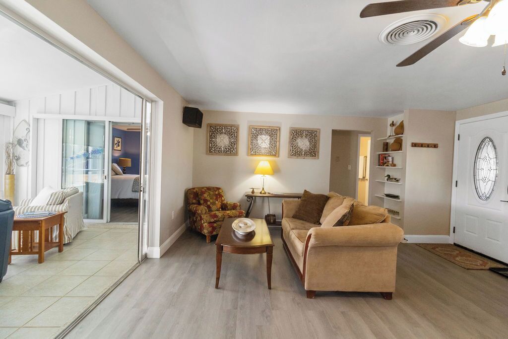 A living room with a sofa, armchair, and coffee table, a ceiling fan, and a door with a decorative glass window.