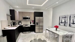 Une cuisine moderne dotée d’un îlot central, d’appareils électroménagers en acier inoxydable et d’un coin repas avec des chaises transparentes.